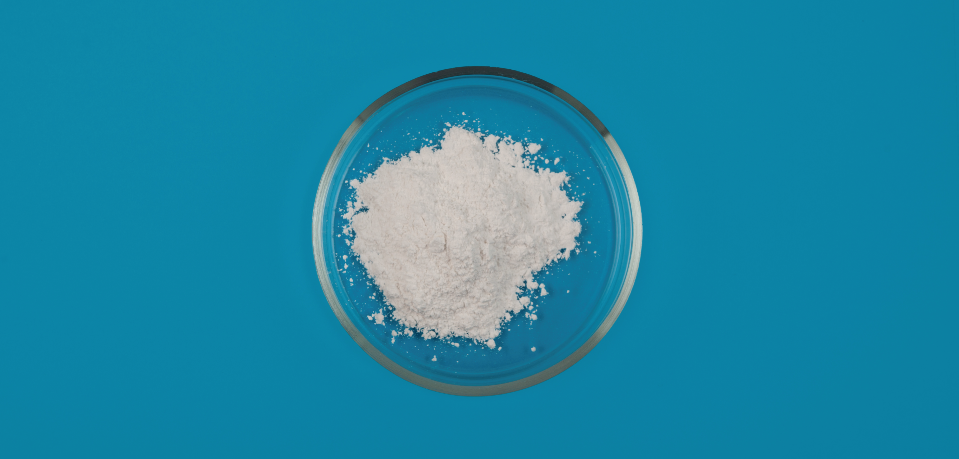 Overhead shot of white powder in a clear bowl on a blue surface top